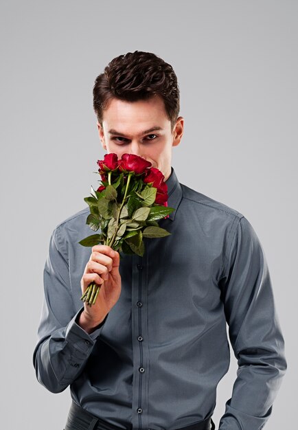 Hombre guapo oliendo ramo de rosas rojas