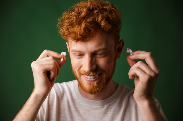 Hombre guapo pelirrojo rizado en camiseta blanca inserte auriculares en sus oídos