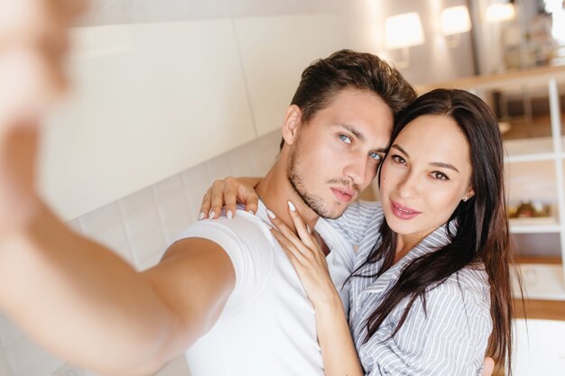 Hombre guapo con pelo corto tomando una foto de sí mismo mientras su novia lo abraza