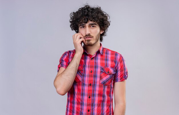 Un hombre guapo pensativo con cabello rizado en camisa a cuadros manteniendo la mano en la cara
