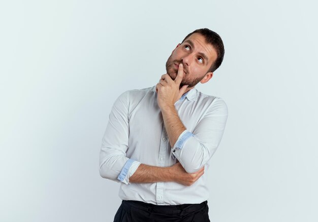 Hombre guapo pensativo pone la mano en la barbilla mirando hacia arriba aislado en la pared blanca