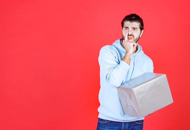 Hombre guapo pensativo sosteniendo su caja de regalo y mirando a otro lado