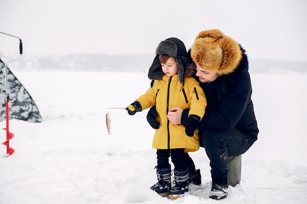 Hombre guapo en una pesca de invierno con su pequeño hijo