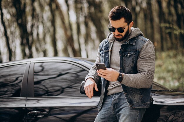 Hombre guapo de pie junto al coche en el parque