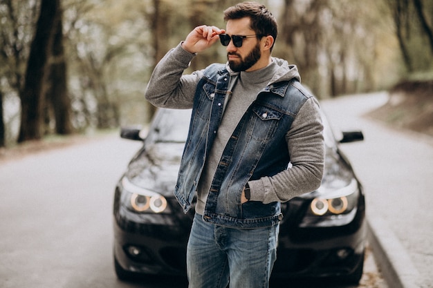 Hombre guapo de pie junto al coche en el parque