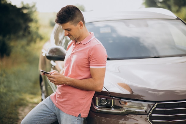 Hombre guapo de pie junto a su automóvil en el bosque