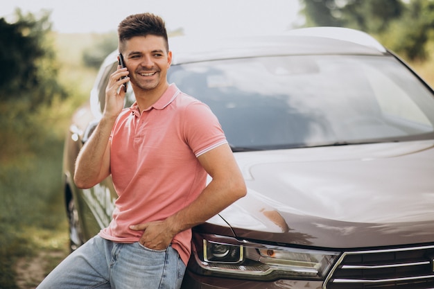 Hombre guapo de pie junto a su automóvil en el bosque