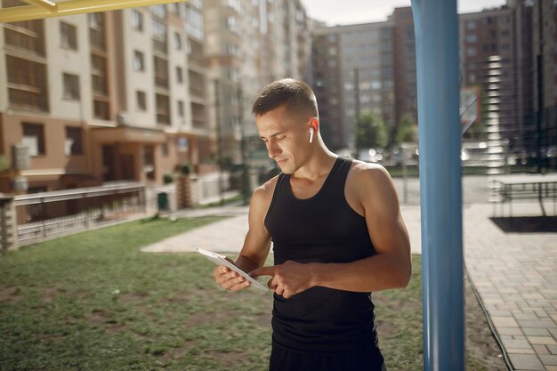Hombre guapo de pie en un parque con auriculares y una tableta
