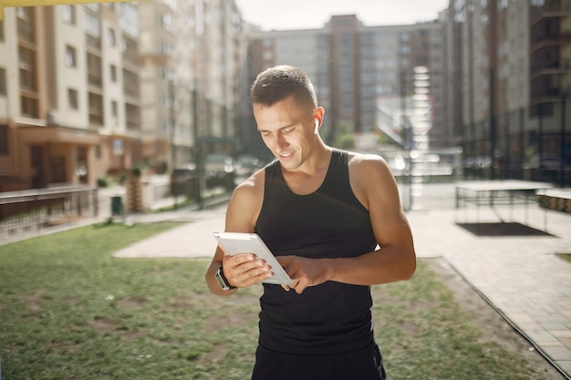 Hombre guapo de pie en un parque con auriculares y una tableta