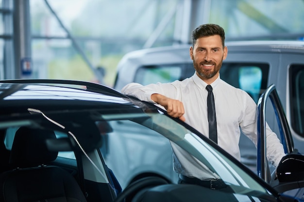 Hombre guapo posando cerca de un coche de lujo en la sala de exposición