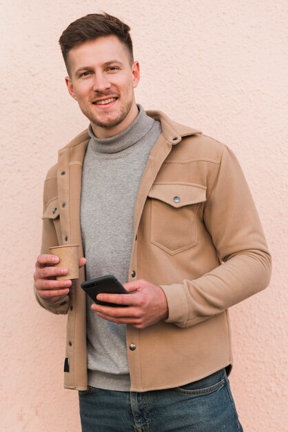 Hombre guapo posando mientras sostiene la taza de café y smartphone