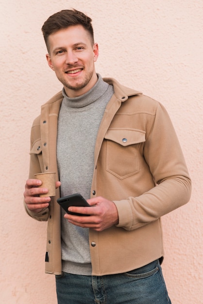 Hombre guapo posando mientras sostiene la taza de café y smartphone