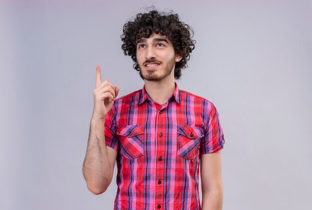 Un hombre guapo positivo con pelo rizado en camisa a cuadros pensando y apuntando hacia arriba