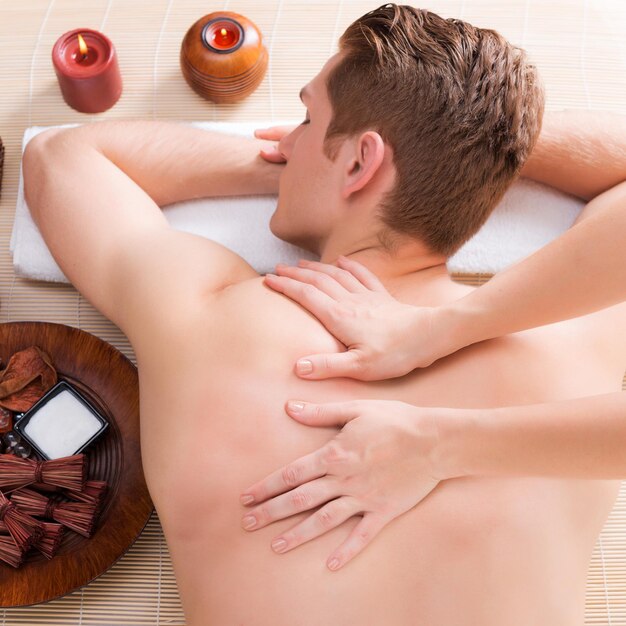 Hombre guapo relajado y disfrutando de un masaje de espalda de tejido profundo en el salón de spa.