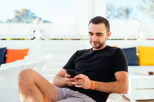 Hombre guapo relajante tuping por teléfono en la playa.