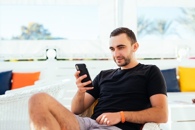 Hombre guapo relajante tuping por teléfono en la playa.