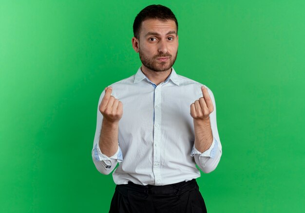 Hombre guapo seguro gestos dinero signo de la mano con las dos manos aisladas en la pared verde