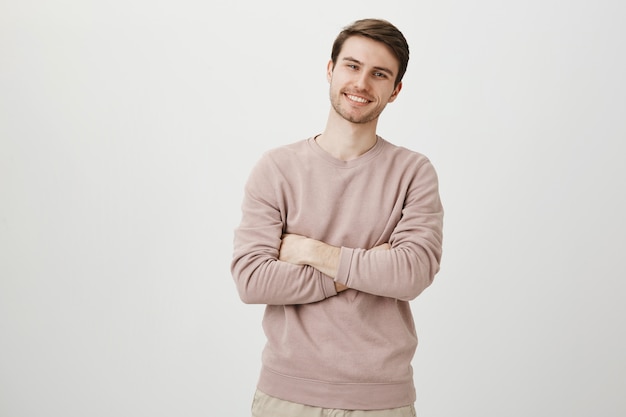 Hombre guapo seguro sonriendo complacido, pecho de brazos cruzados