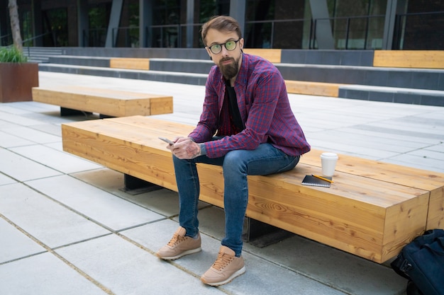 Hombre guapo sentado en un banco de madera con teléfono