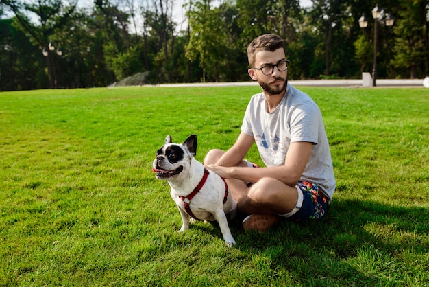 Hombre guapo sentado con bulldog francés sobre césped en el parque