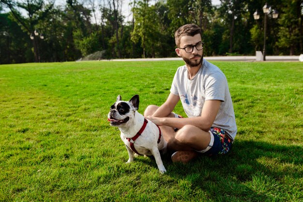 Hombre guapo sentado con bulldog francés sobre césped en el parque