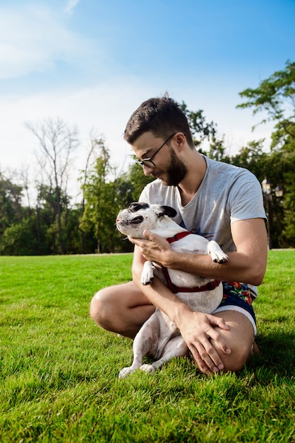 Hombre guapo sentado con bulldog francés sobre césped en el parque