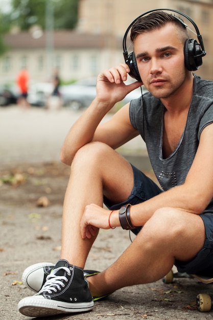 Hombre guapo sentado en la calle con auriculares