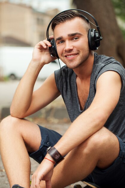 Hombre guapo sentado en la calle con auriculares