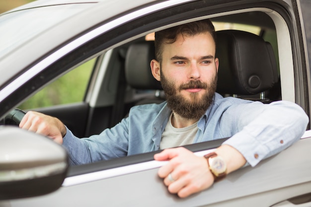 Hombre guapo sentado en el coche mirando por la ventana