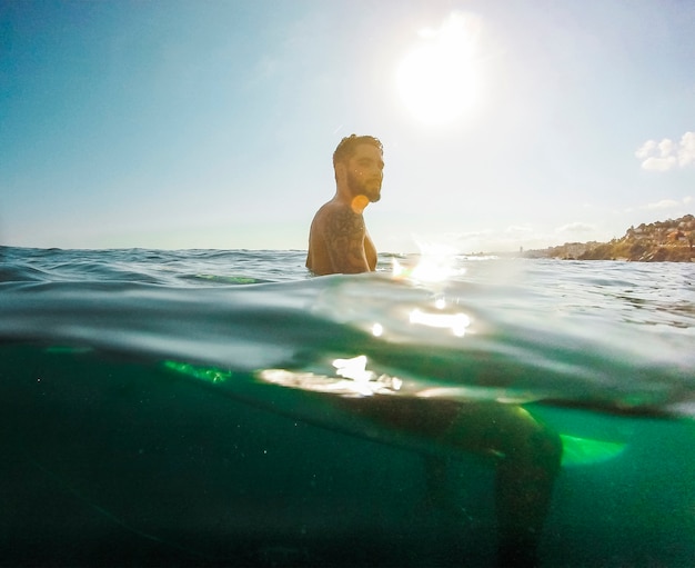 Foto gratuita hombre guapo sentado en la tabla de surf en el mar