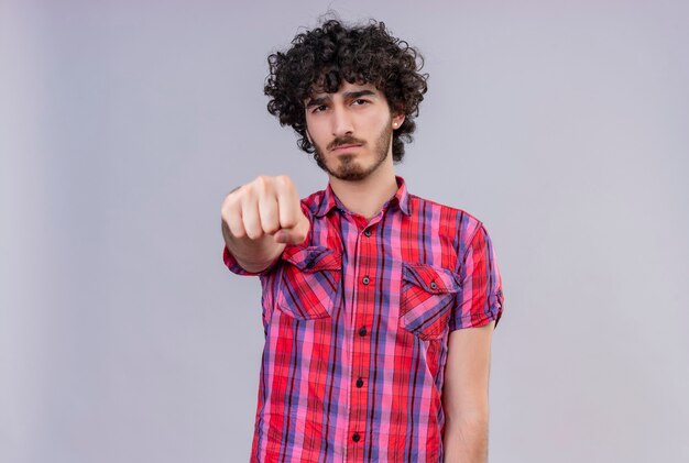 Un hombre guapo serio con el pelo rizado en camisa a cuadros mostrando el puño cerrado