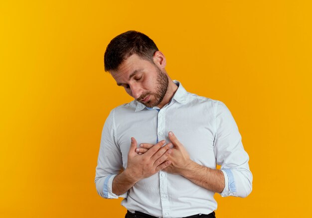 Hombre guapo soñoliento pone las manos en el pecho aislado en la pared naranja