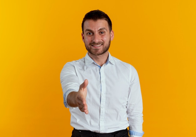 Hombre guapo sonriente extiende la mano aislada en la pared naranja