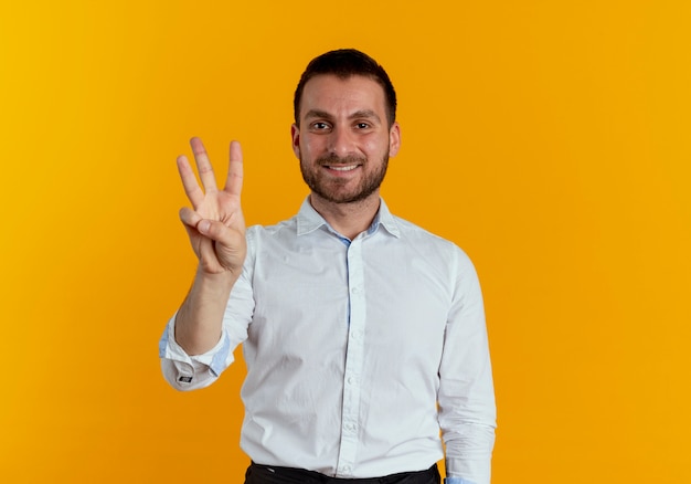 Foto gratuita hombre guapo sonriente gesticula tres con los dedos aislados en la pared naranja