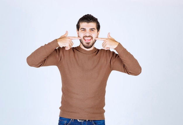 Hombre guapo sonriente gesticulando y señalando con los dientes. Foto de alta calidad