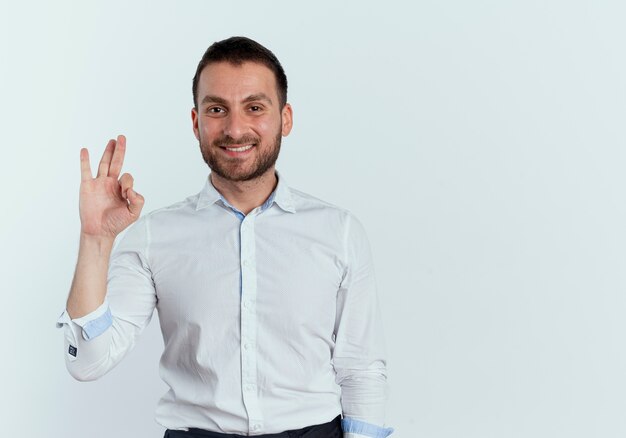 Hombre guapo sonriente gestos ok signo de mano aislado en la pared blanca