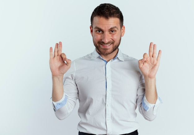 Hombre guapo sonriente gestos ok signo de mano aislado en la pared blanca