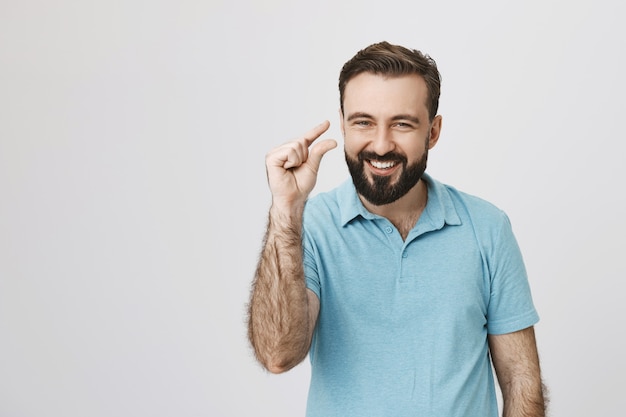 Hombre guapo sonriente mostrando algo pequeño o pequeño