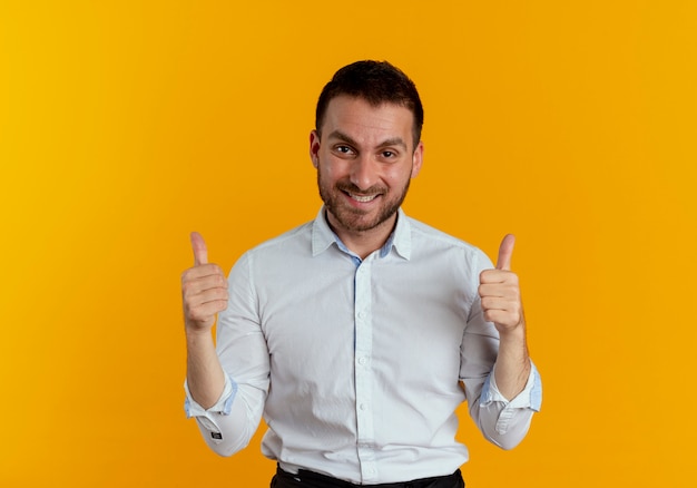 Hombre guapo sonriente pulgares arriba con las dos manos aisladas en la pared naranja