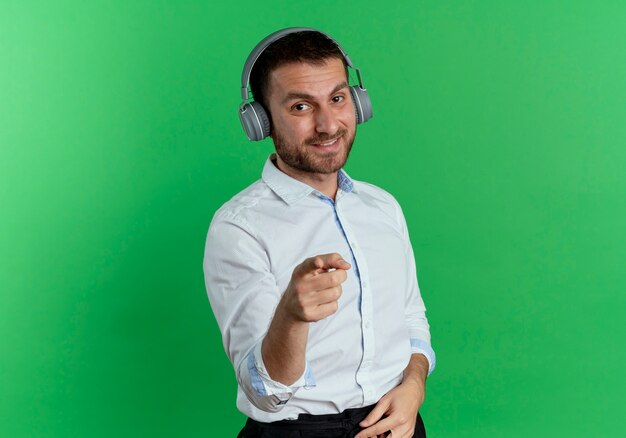 Hombre guapo sonriente en puntos de auriculares aislados en la pared verde