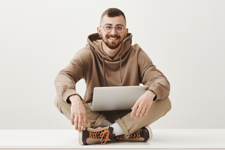 Foto gratuito hombre guapo sonriente sentarse sobre las piernas cruzadas con el portátil
