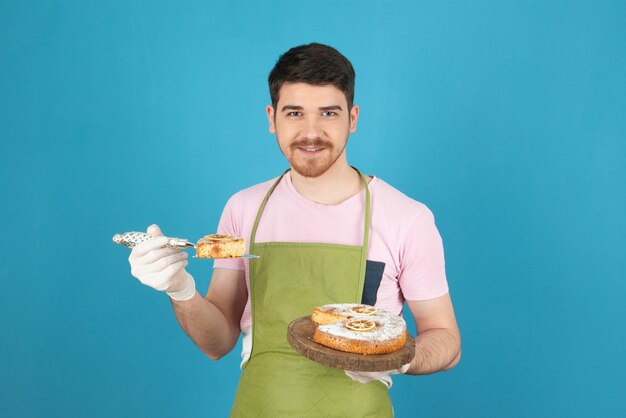 Hombre guapo sonriente sosteniendo una rebanada de pastel y mirando a la cámara.