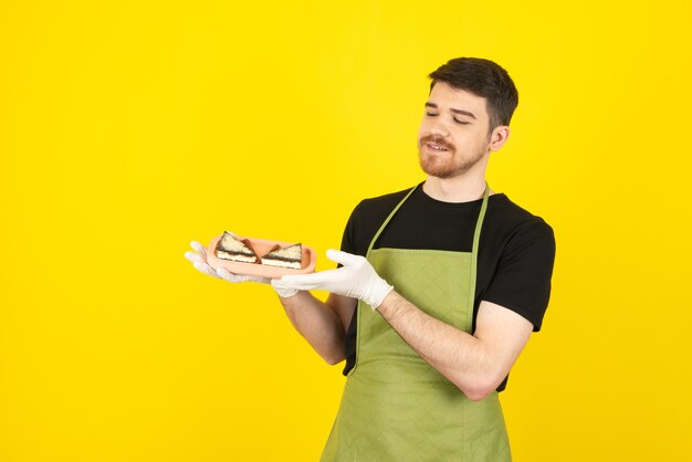 Hombre guapo sonriente sosteniendo rebanadas de pastel fresco en un amarillo.