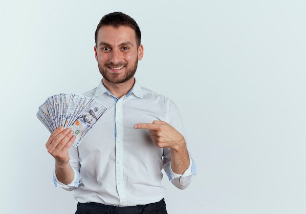 Foto gratuita hombre guapo sonriente sostiene y apunta a dinero aislado en la pared blanca