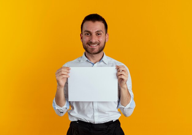 Hombre guapo sonriente sostiene la hoja de papel aislada en la pared naranja