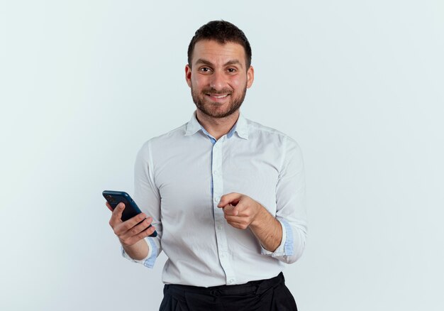 Hombre guapo sonriente sostiene teléfono y puntos aislados en la pared blanca