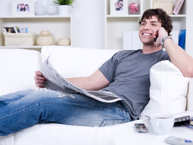 Hombre guapo sonriente con teléfono y periódico - acostado en casa