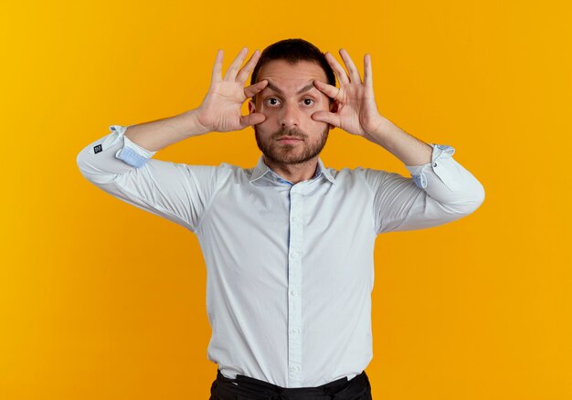 Hombre guapo sorprendido abre los ojos con los dedos aislados en la pared naranja