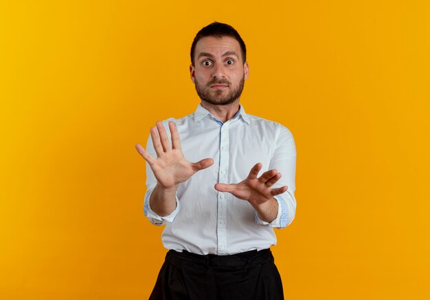 Hombre guapo sorprendido se encuentra con las manos levantadas mirando aislado en la pared naranja