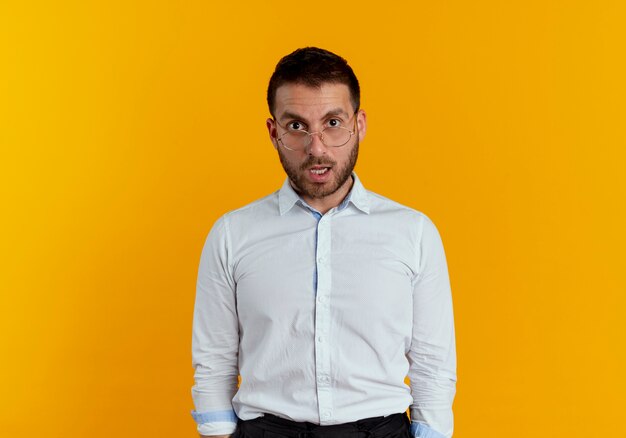 Hombre guapo sorprendido con gafas ópticas se ve aislado en la pared naranja